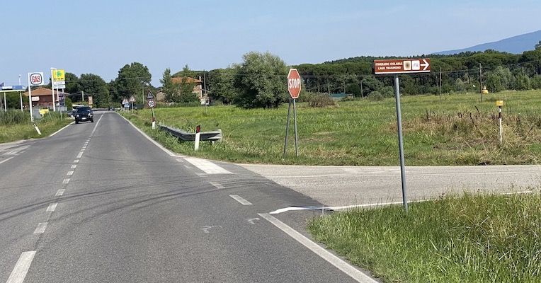 Cartello stradale che indica l'accesso alla Ciclovia del Trasimeno, vicino a un bivio sulla SR142 in un'area rurale.