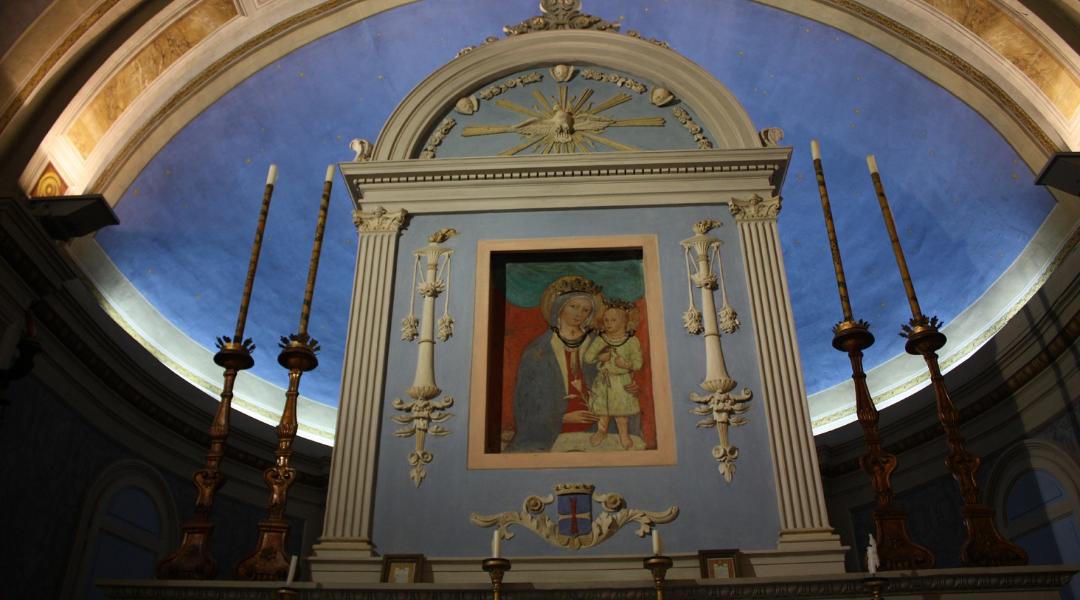 Altar with an image of the Madonna and Child, framed by columns and candleholders, under a semi-circular blue vault.