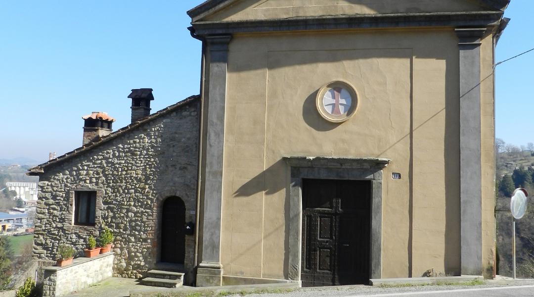 Facade of a church with a wooden door topped by a small central rose window with a Greek cross emblem.