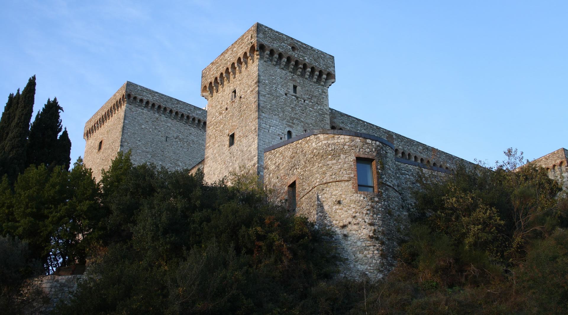 Vista laterale dal basso della Rocca di Narni, con le sue torri merlate e le mura in pietra che emergono sopra la vegetazione