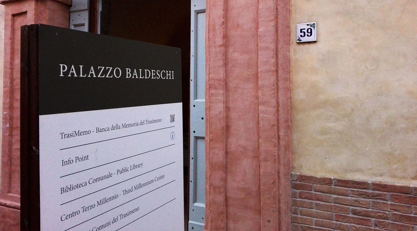 View of the entrance door of Palazzo Baldeschi, with an information board in the foreground providing details about the palace and its activities.