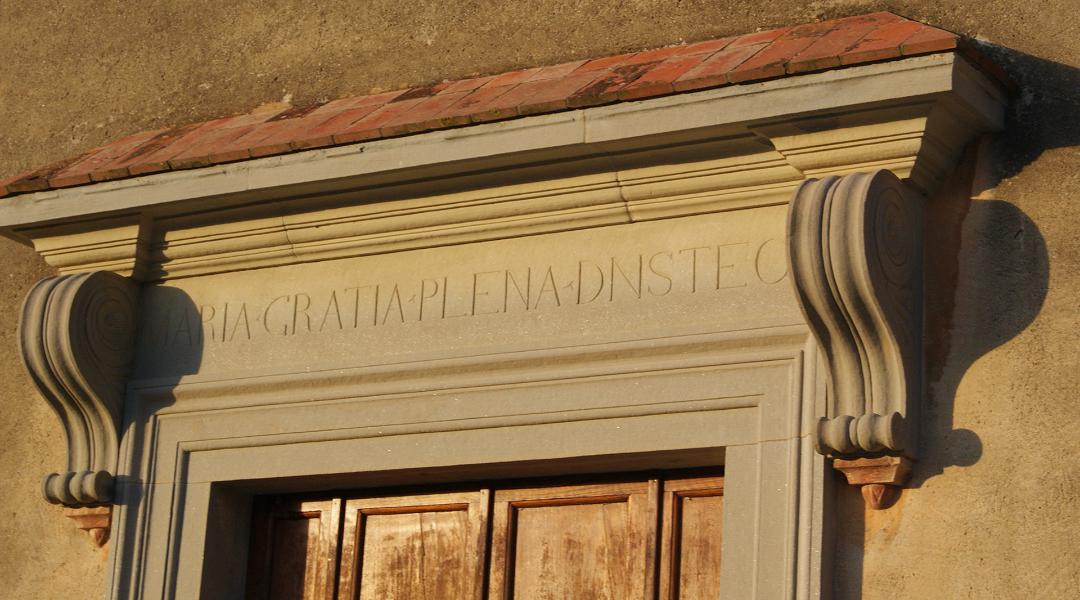 Portail en pierre avec une inscription au-dessus d'une porte en bois, décoré de volutes latérales.