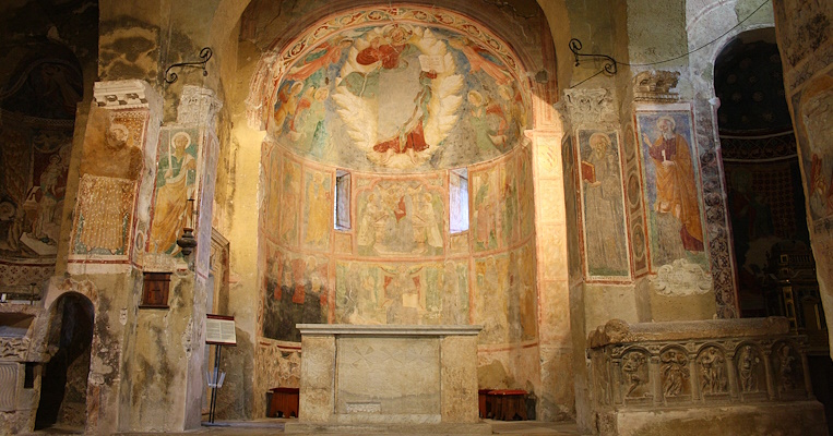 Vista su un’abside riccamente decorato con affreschi raffiguranti scene religiose e sull'altare maggiore dell'abbazia, semplice e centrale, con una struttura in marmo.