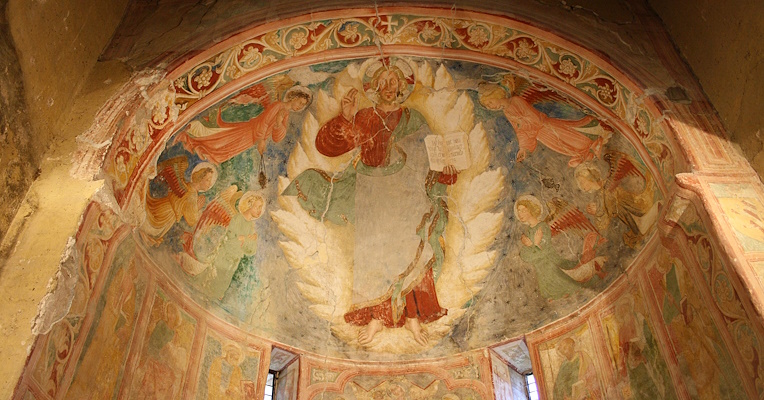 Abside decorato con un affresco che raffigura una scena religiosa con figure angeliche e santi, circondati da motivi floreali e decorativi.with a fresco depicting a religious scene with angelic figures and saints, surrounded by floral and decorative motifs.