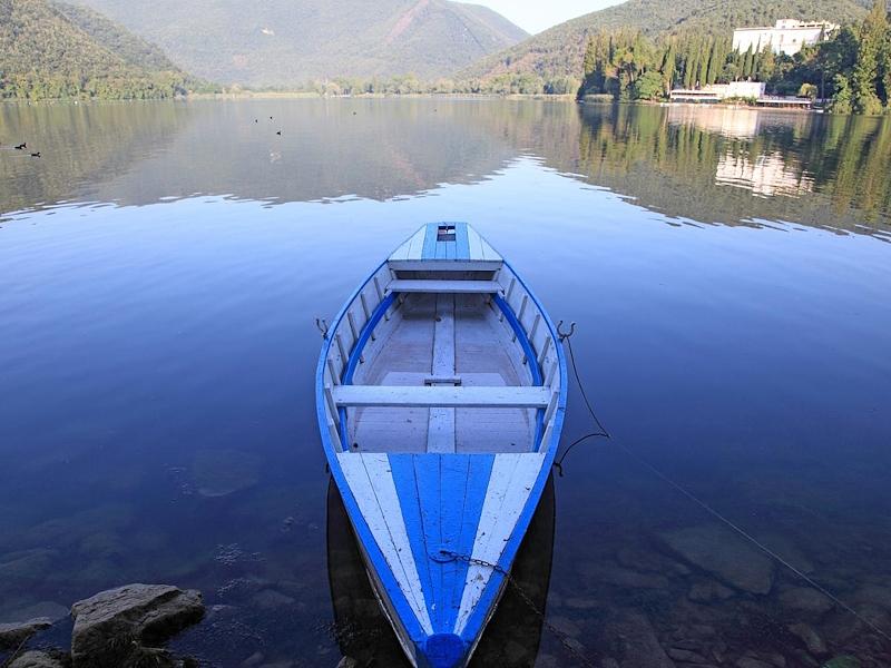 Am Ufer festgemachtes Boot auf dem ruhigen Lago di Piediluco mit spiegelnden Bergen im Hintergrund.