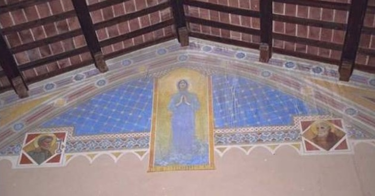 Fresco with a central praying Madonna on a star-decorated blue background, flanked by two saintly figures, under a wooden beam ceiling.