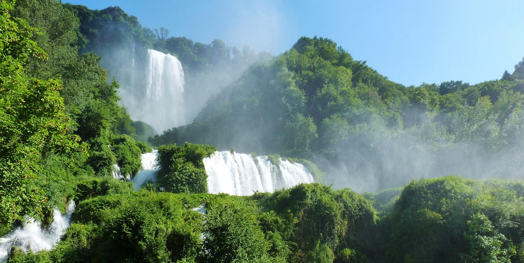 La Cascata delle Marmore vista dal basso: salti d’acqua tra fitte vegetazioni, spruzzi e vapore che si alzano verso il cielo limpido.