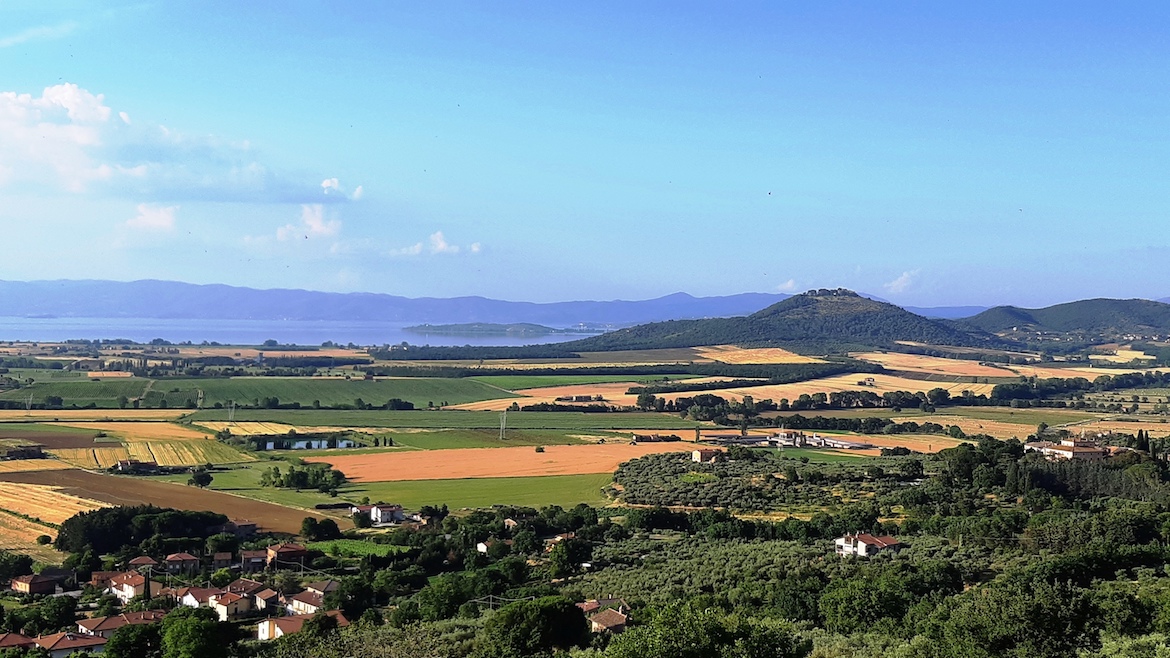 Panorama from Panicale: view over stretches of cultivated fields and green hills with Lake Trasimeno in the background.