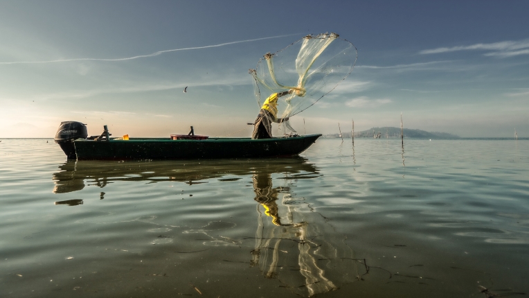 Pêcheurs à bord d'un bateau sur le lac Trasimène en train de lancer un filet pour attraper du poisson