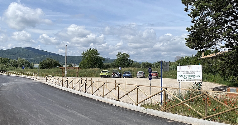 Rest and parking area at Oasi La Valle (La Valle Nature Reserve), with views of hills and parked cars.