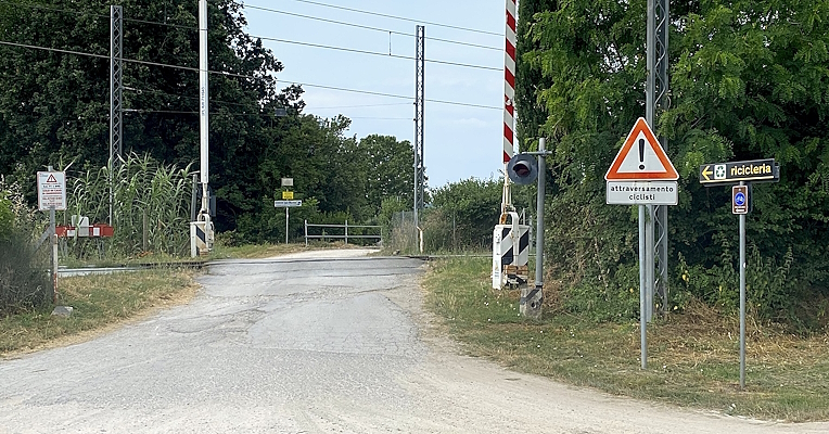 Bahnübergang mit Verkehrsschildern, Warnung vor Zugüberquerungen und Hinweisen zum Recyclinghof entlang eines Schotterwegs.