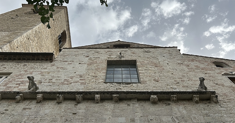 Ansicht von unten der Fassade der ehemaligen Kirche San Domenico in Narni, jetzt Bortolotti Auditorium. Die Steinfront ist durch ein großes rechteckiges Fenster und einen quer verlaufenden Rahmen von Masken, die als Karyatiden dienen, gekennzeichnet, während sich auf beiden Seiten des Fensters über dem Rahmen zwei Steinlöwen befinden.