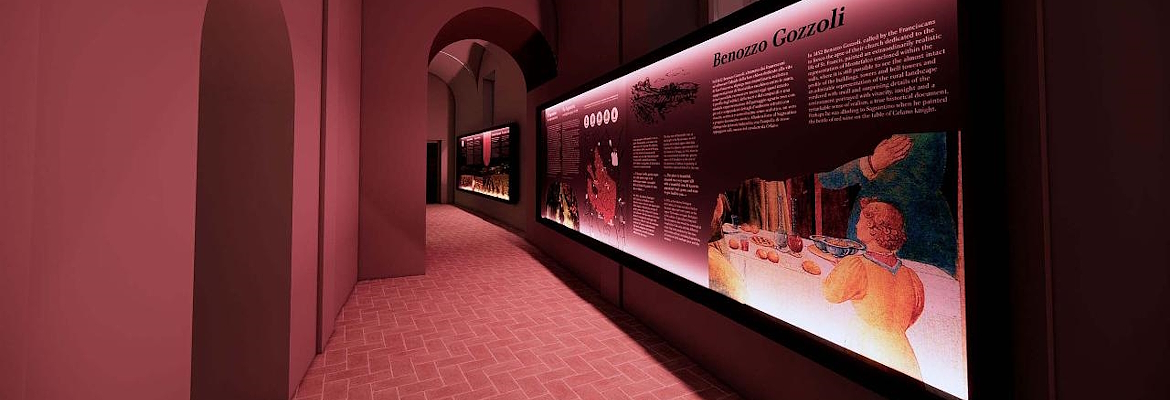 A museum corridor with walls and arches illuminated by a dark pink light. On the right, a long informational panel features texts and images dedicated to Benozzo Gozzoli.