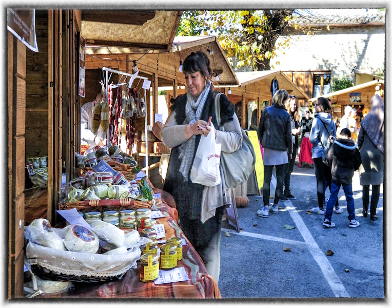 Groupe de personnes visitant l'exposition du marché des produits de la forêt et du sous-bois, avec une attention particulière pour un exposant de miel, de fromage et de charcuterie.