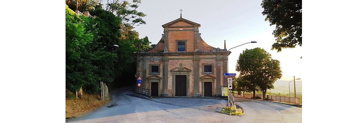 A small brick church, surrounded by trees, is located at a crossroads with street signs.