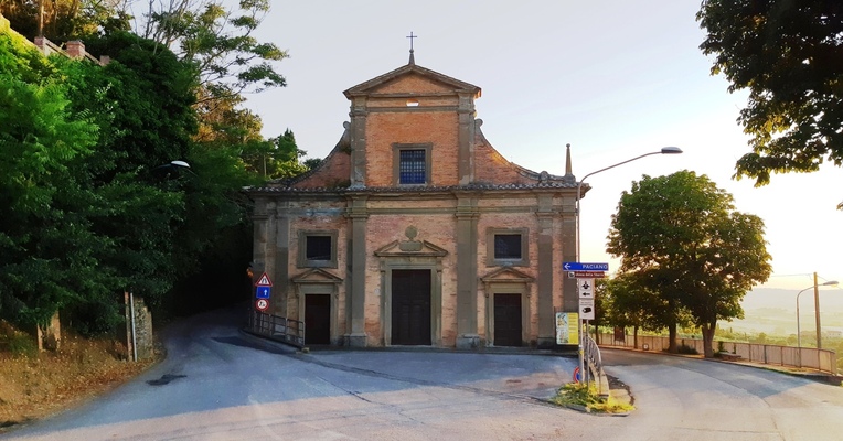  A small brick church, surrounded by trees, is located at a crossroads with street signs. 