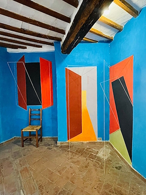 Room with blue walls, red and black geometric decorations, and a wooden chair against the wall.