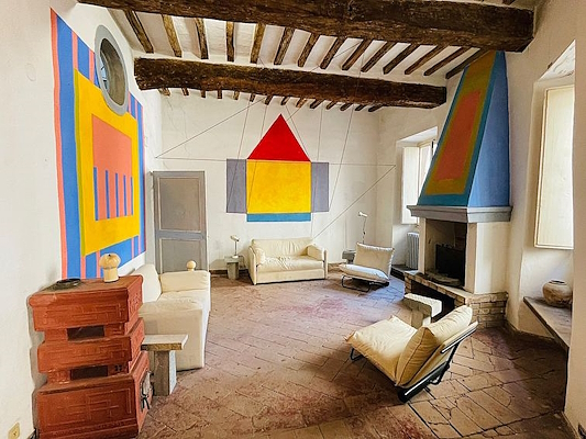 Living room with beamed ceiling, colorful geometric wall designs, a fireplace, and light-colored sofas and chairs.