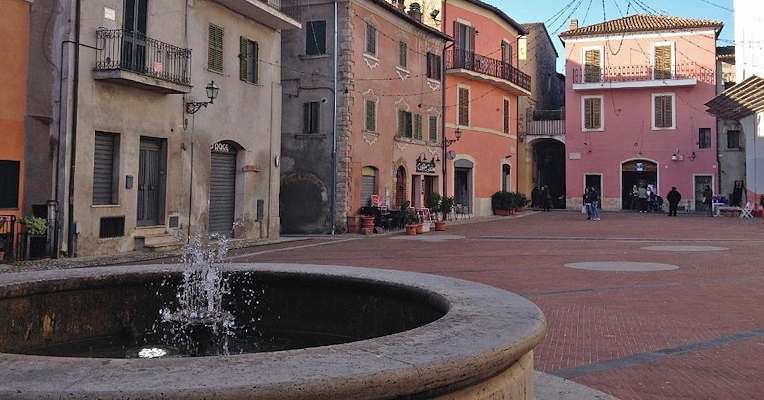 View of the Piazza di Cesi with houses of different colours and a fountain in the centre with gushing water