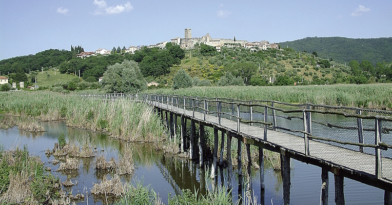 Un ponte attraversa l’oasi naturalistica, mentre sullo sfondo, in cima alla collina, si distinguono le antiche strutture medievali del castello di San Savino