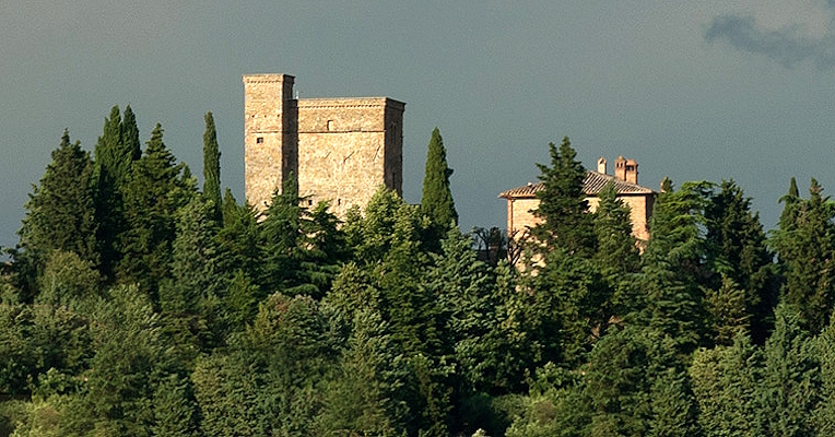 In lontananza, le torri di Rocca Monaldi si ergono sopra un panorama di fitti boschi, creando una scena suggestiva.