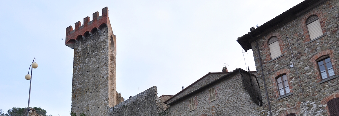 Medieval stone tower with red battlements, surrounded by stone buildings with arched windows and brick details.