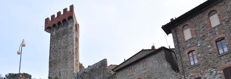 Titolo: Torre medievale in pietra con merlature rosse, circondata da edifici in pietra con finestre ad arco e dettagli in mattoni. 