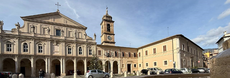 Immagine: La facciata della Cattedrale di Santa Maria Assunta a Terni, con il suo portico colonnato e la torre campanaria laterale, con la fontana antistante che riflette il cielo e il palazzo adiacente la cattedrale 