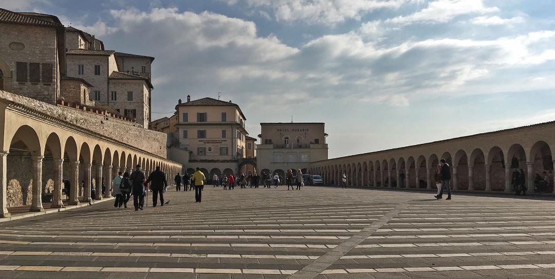 View of the square in front of the Basilica of St. Francis in Assisi, characterised by wide stone porticoes on both sides.