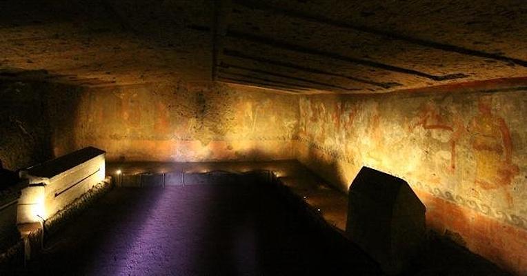 Interior of the Tomb of the Hescanas with gabled roof and illuminated bench with sarcophagi and urns