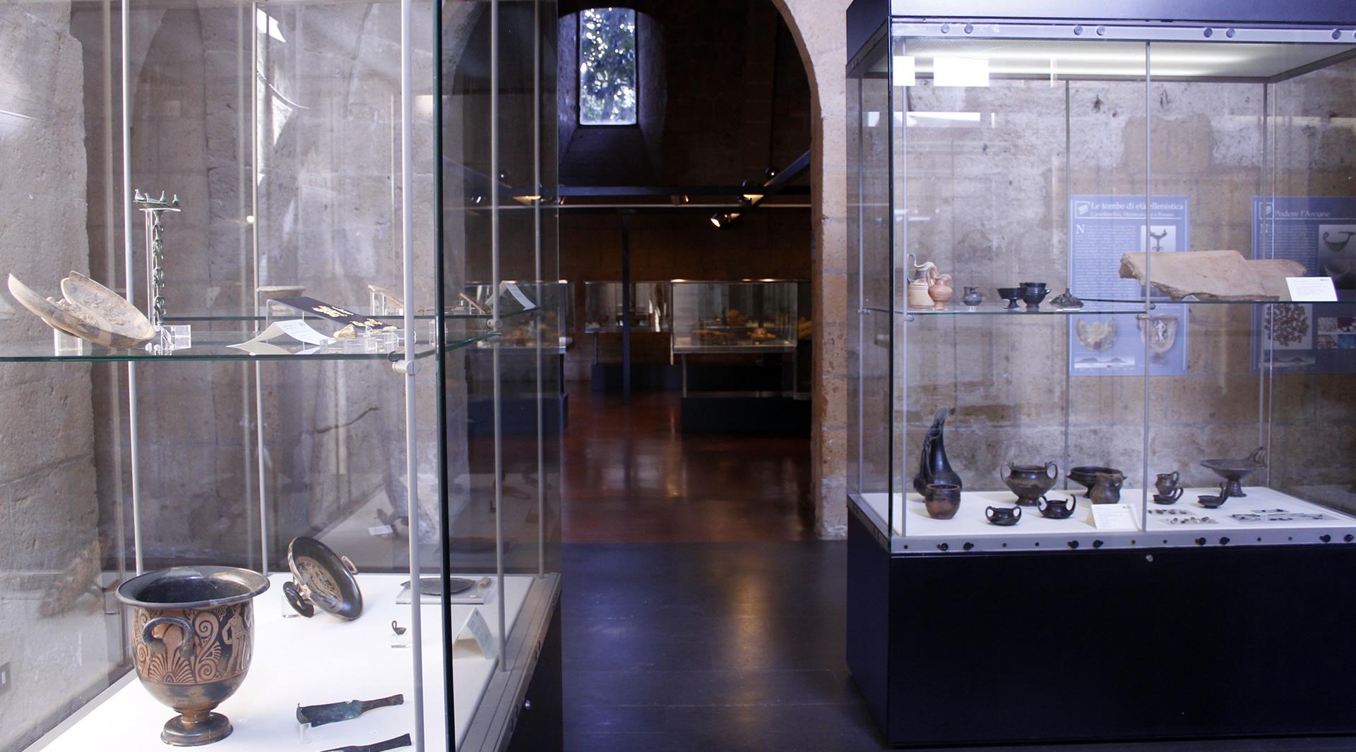 Une salle d'exposition avec des vitrines contenant divers artefacts archéologiques, en particulier des objets en céramique bucchero noir lustré.