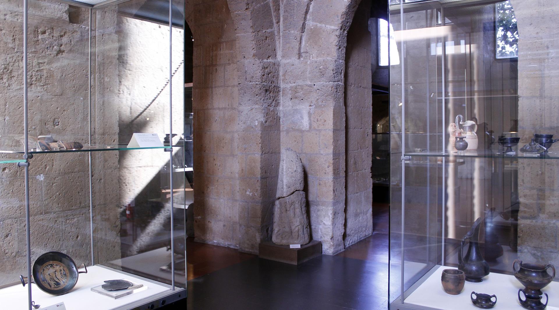 Une salle d'exposition avec des vitrines contenant divers artefacts archéologiques, en particulier des objets en céramique bucchero noir lustré.