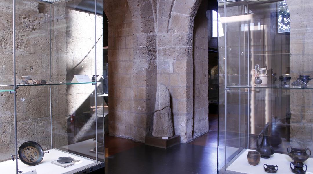 An exhibition room with showcases containing various archaeological artifacts, particularly glossy black bucchero ceramic objects.