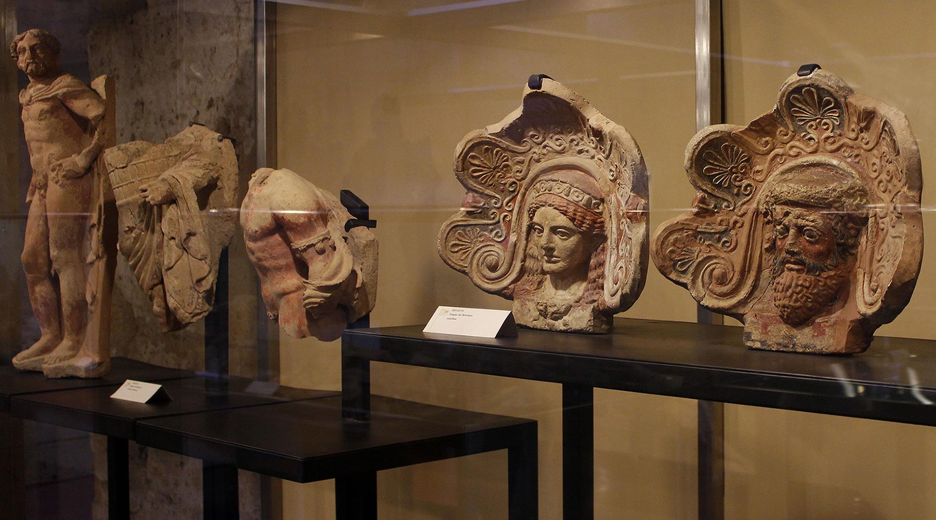 Diverses sculptures étrusques en terre cuite et des antéfixes exposées dans une vitrine.