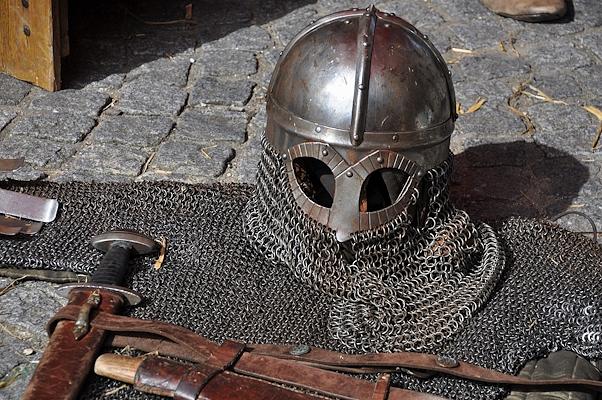 Heaume et cotte de mailles médiévales posés sur un sol en pierre, avec épée et ceinture en cuir